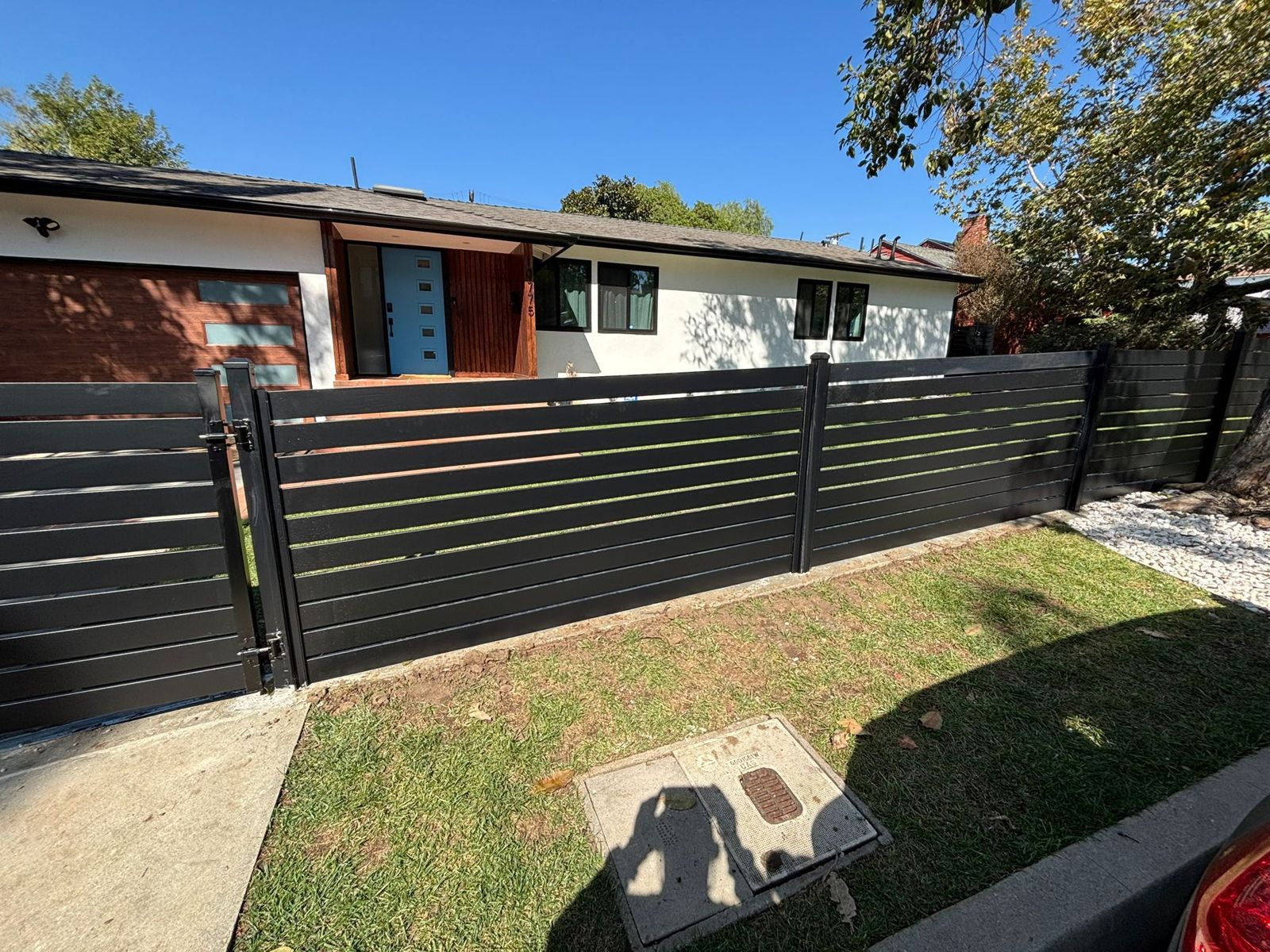 Black horizontal aluminum fence and gate across a front yard