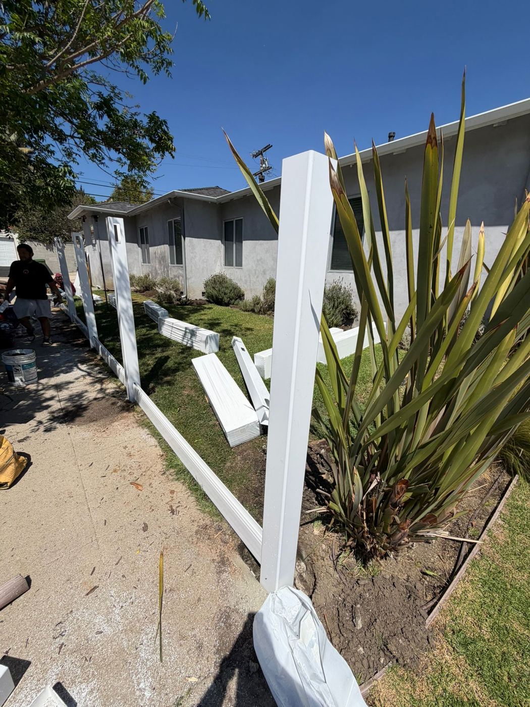 Vinyl fence posts and bottom rails being installed along a sidewalk